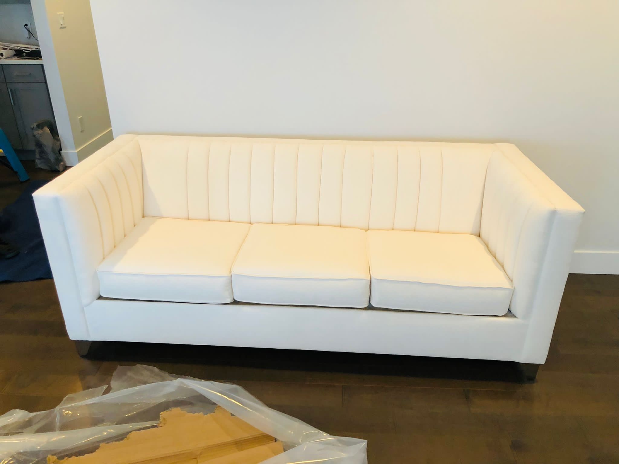 White modern three-seater sofa with vertical stitching on the backrest.