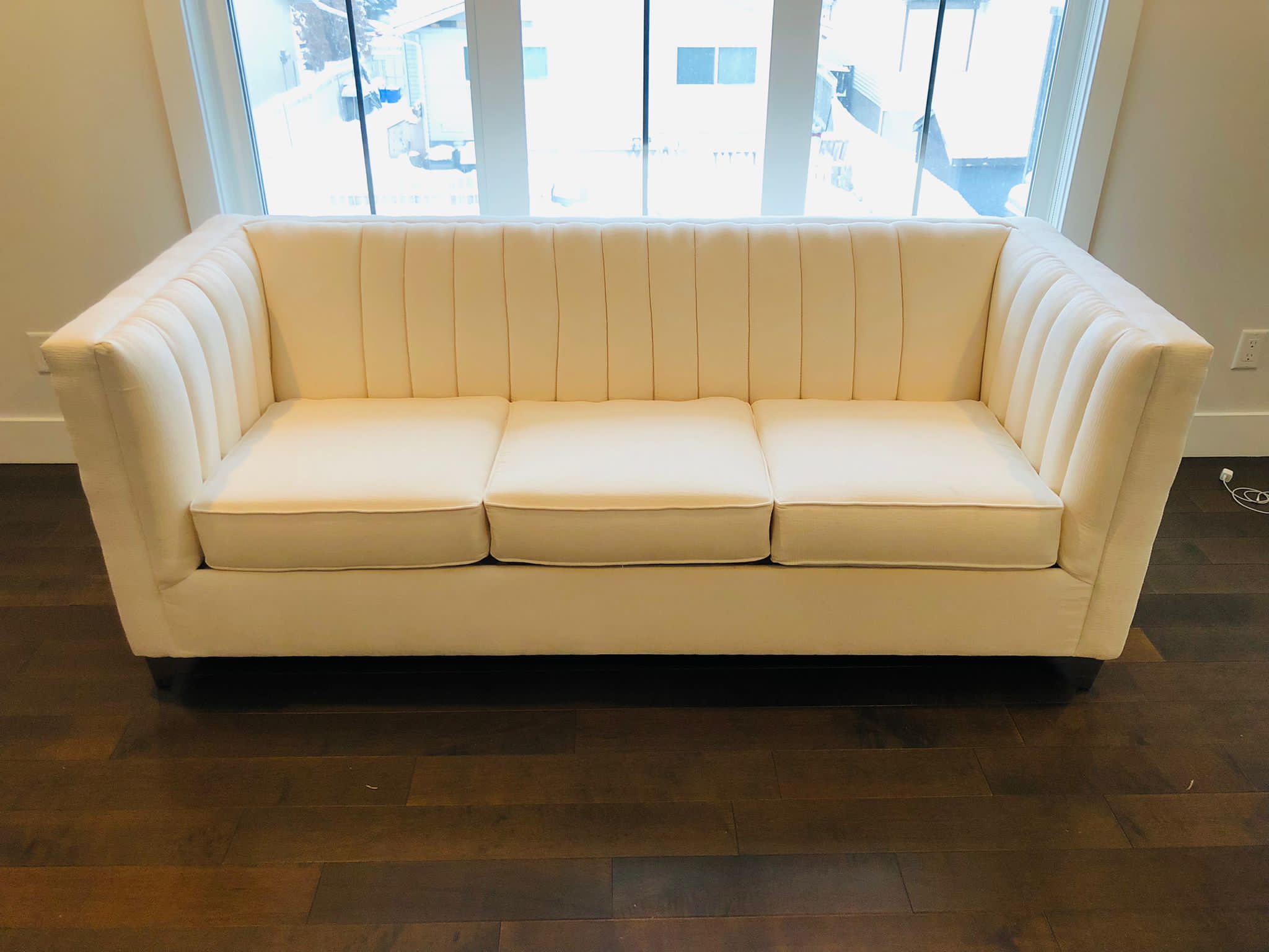 Cream-colored modern sofa near large windows with sunlight.