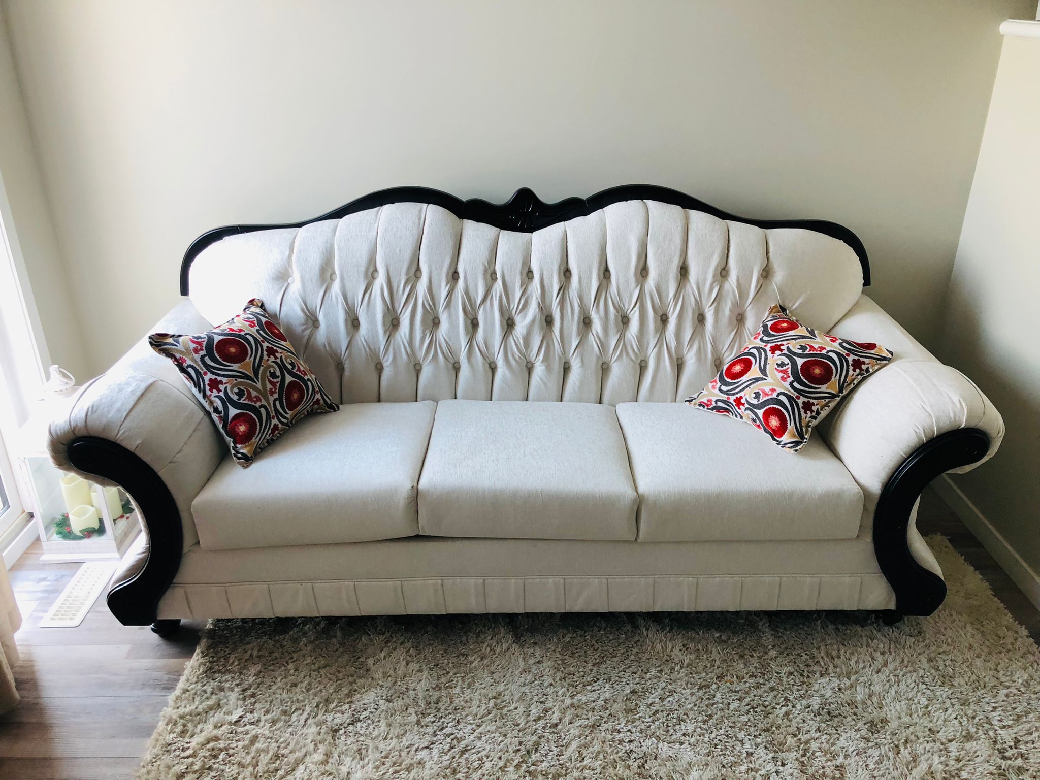 White tufted sofa with black trim and two patterned red and black pillows on a light rug.