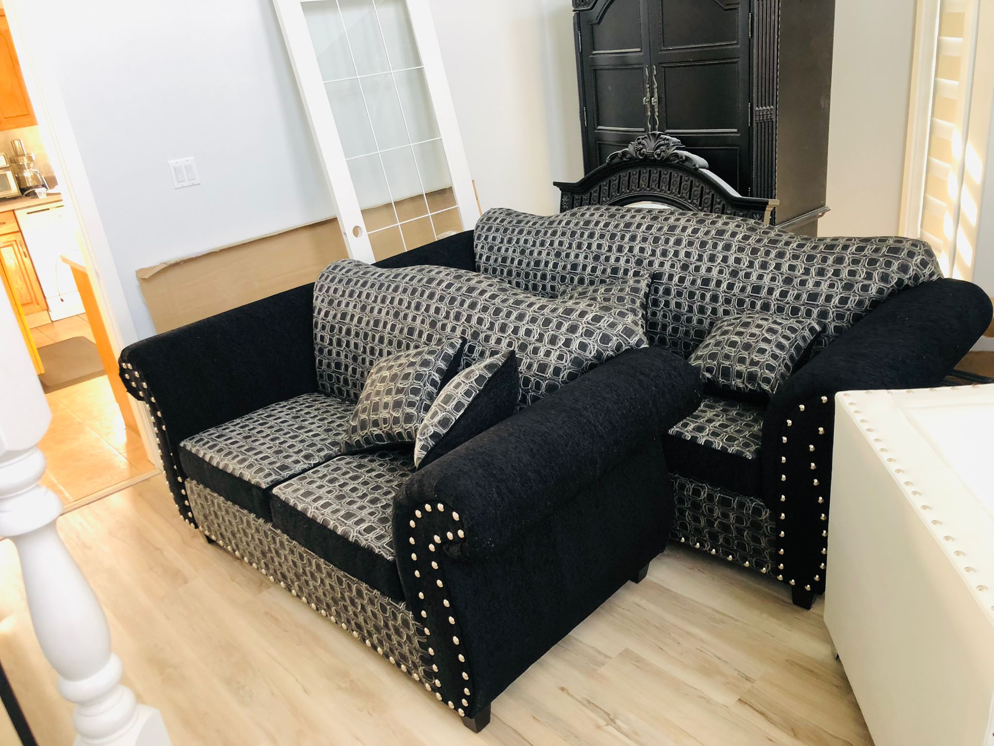 Black and patterned upholstered sofa set with studded arms and matching pillows in a living room.