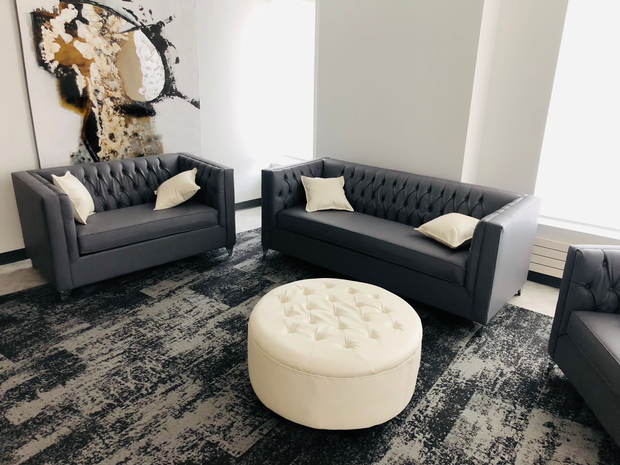 Gray tufted sofas with white pillows and a round white ottoman in a modern living room.